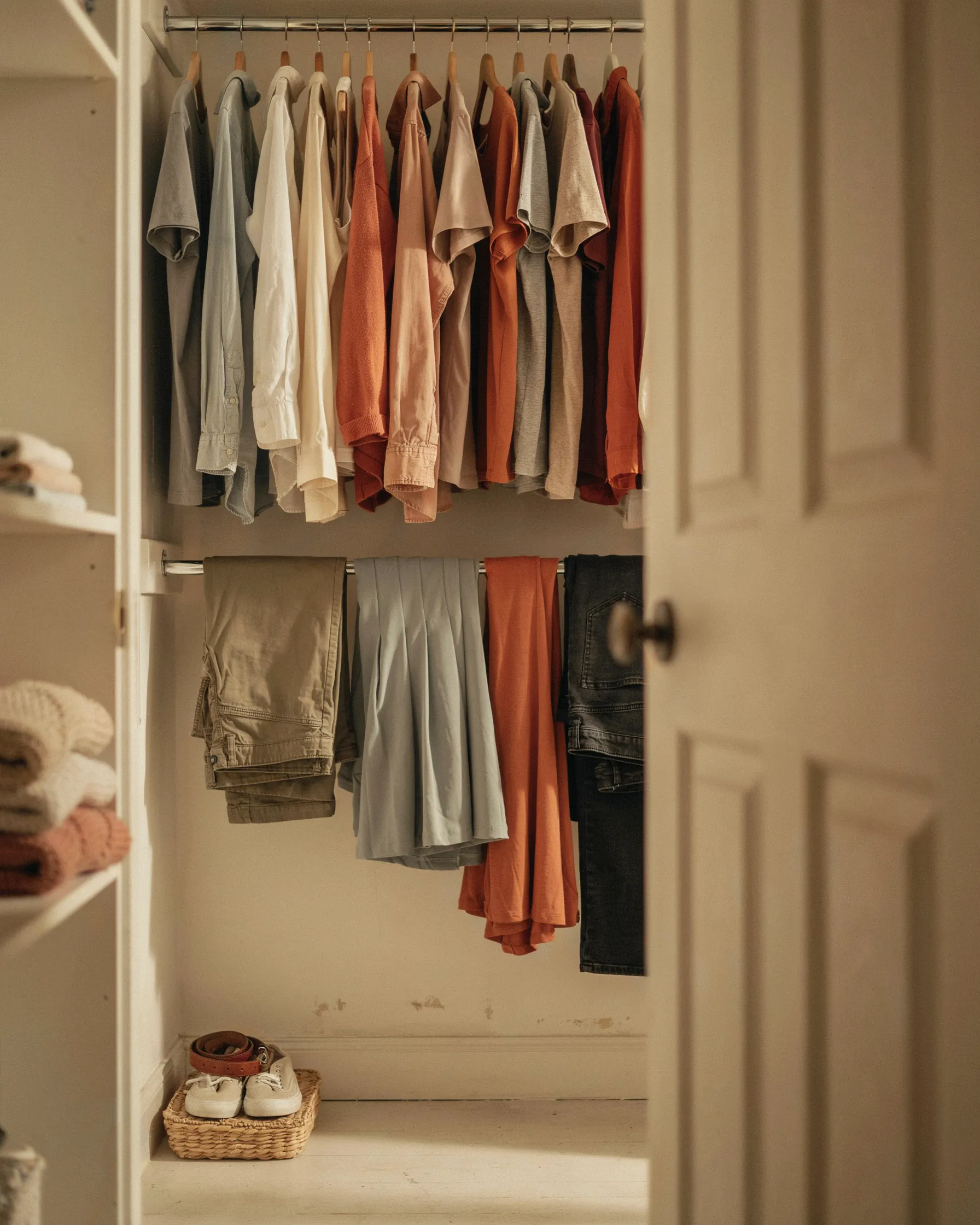 Dorm closet with two rods, shirts hanging above and pants and skirts hanging from a lower tension rod